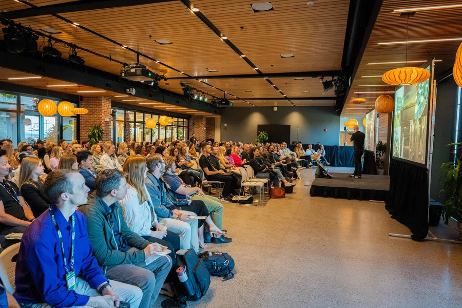 A packed conference audience under warm pendant lights