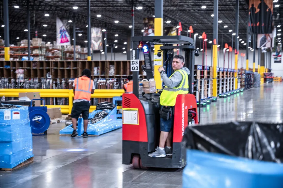 A pallet-jack operator moving through a warehouse aisle
