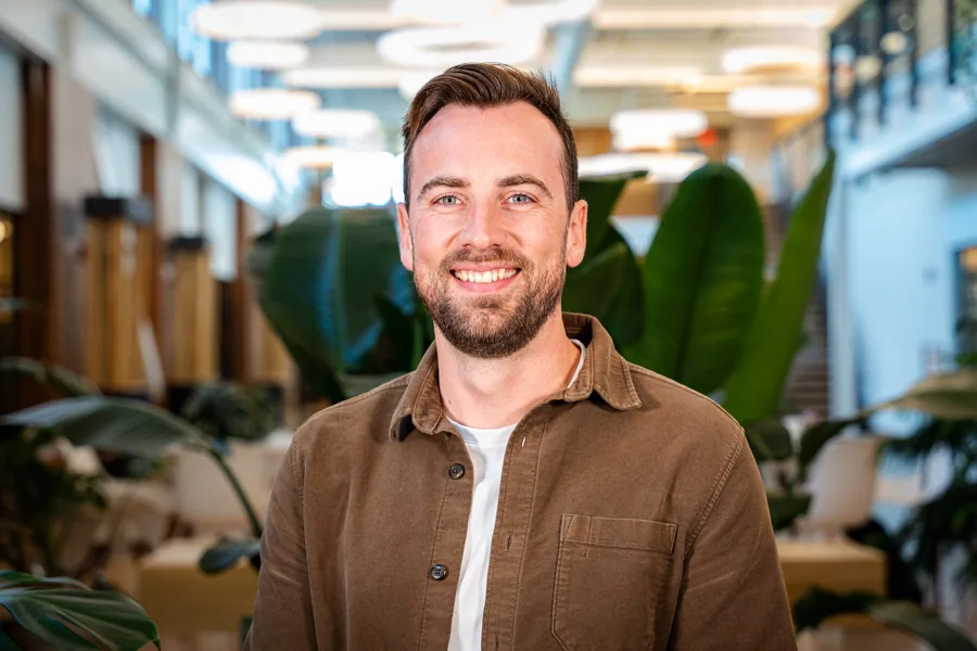 A guest in a brown overshirt smiling for an event headshot