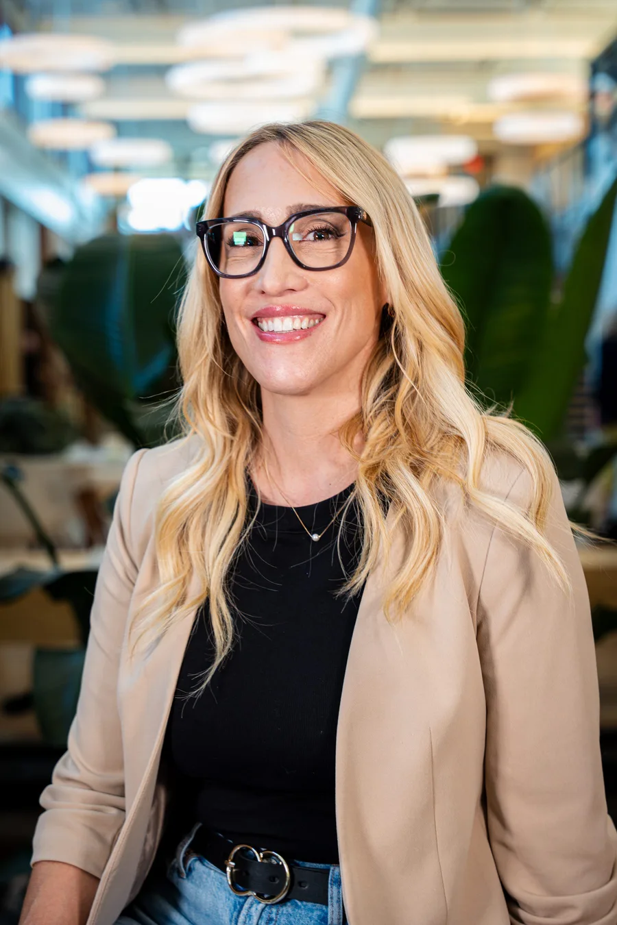A guest wearing a tan blazer and glasses posing for a headshot