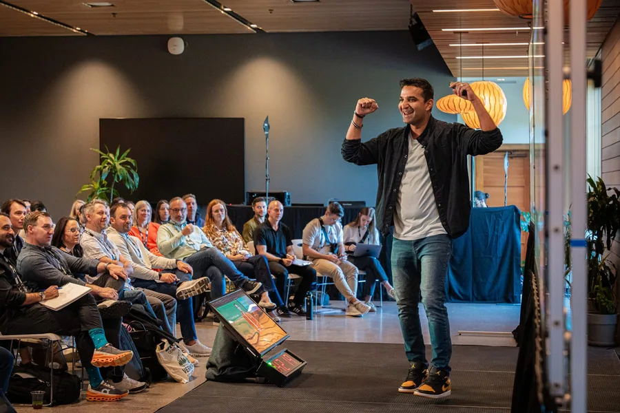 A speaker smiling and raising his hands in front of the conference audience